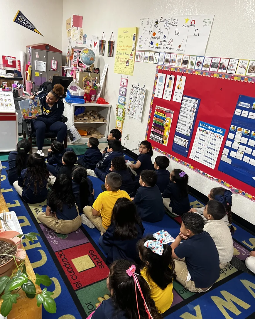Amayah Garcia reading a picture book aloud to a classroom of young students sitting on a rug.