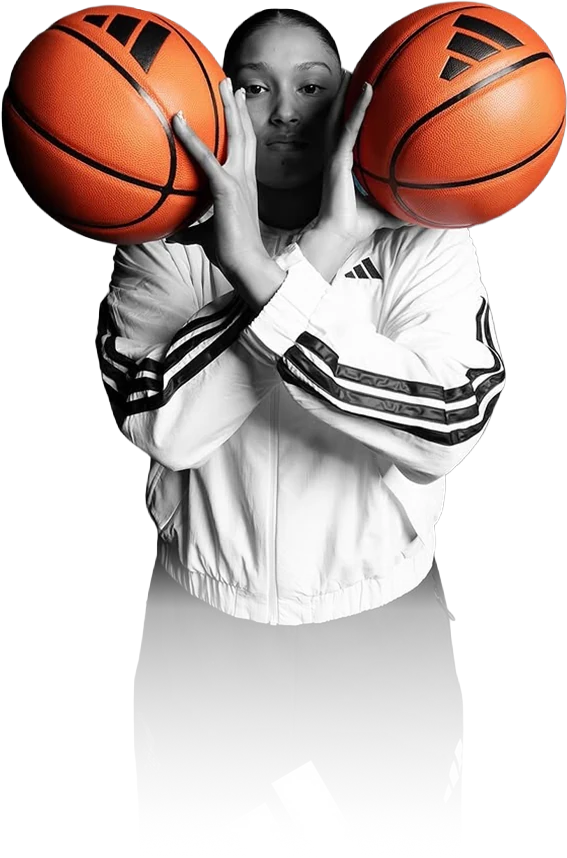 Amayah Garcia holding two basketballs up beside her face in a white adidas jacket, in black and white with only the basketballs in color.