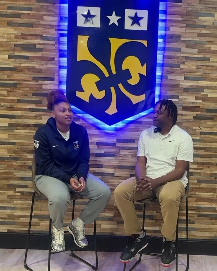 Amayah Garcia sitting on a stool in a Nike quarter-zip, talking to an interviewer in front of a fleur-de-lis banner.