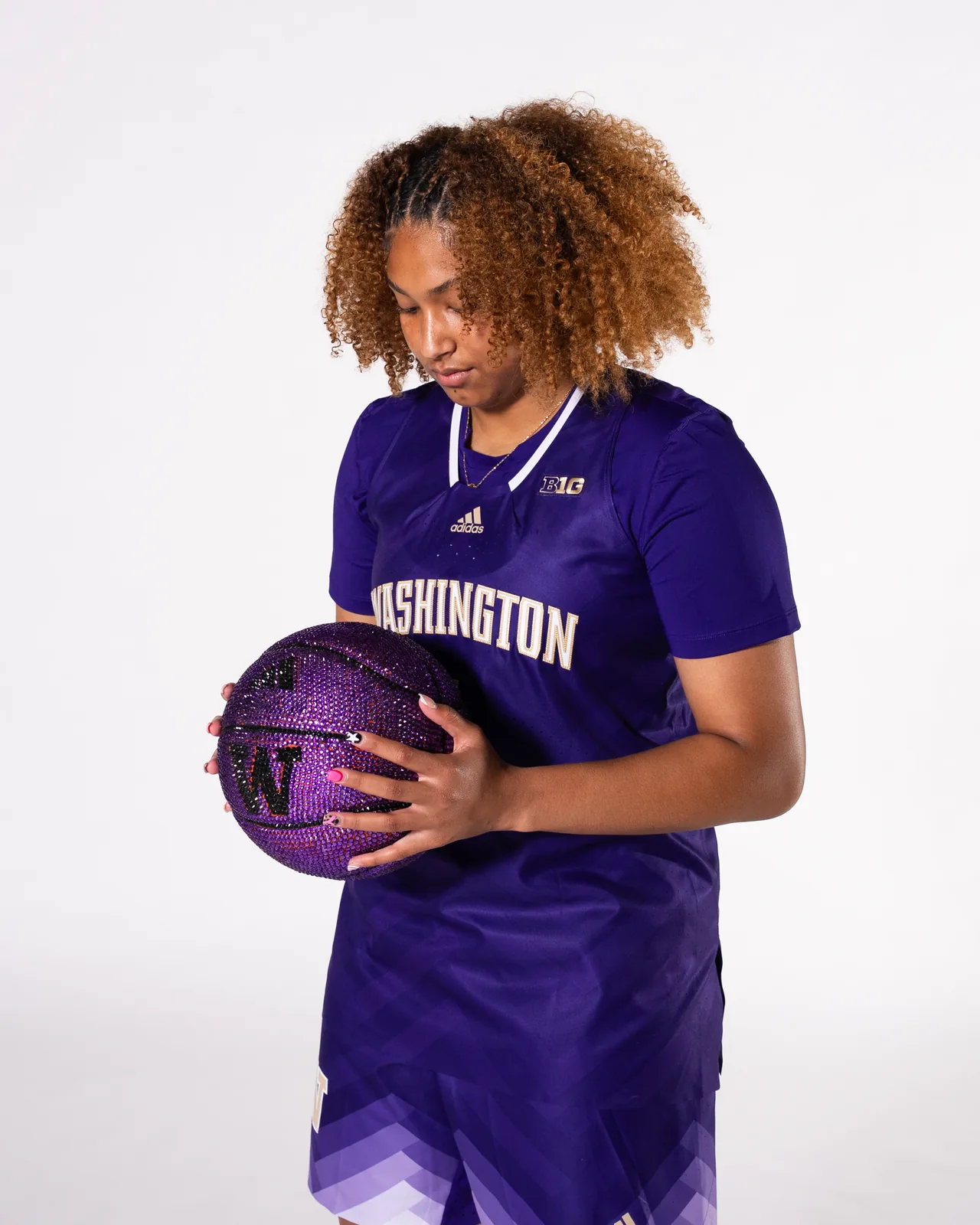 Amayah Garcia in her purple Washington jersey, cradling a crystal basketball and looking down in focus.