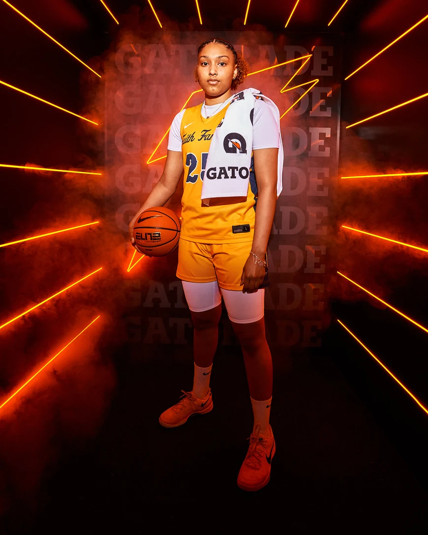 Amayah Garcia in her gold Faith Family number 25 uniform with a Gatorade towel over her shoulder, lit by orange rays at a Gatorade photo shoot.