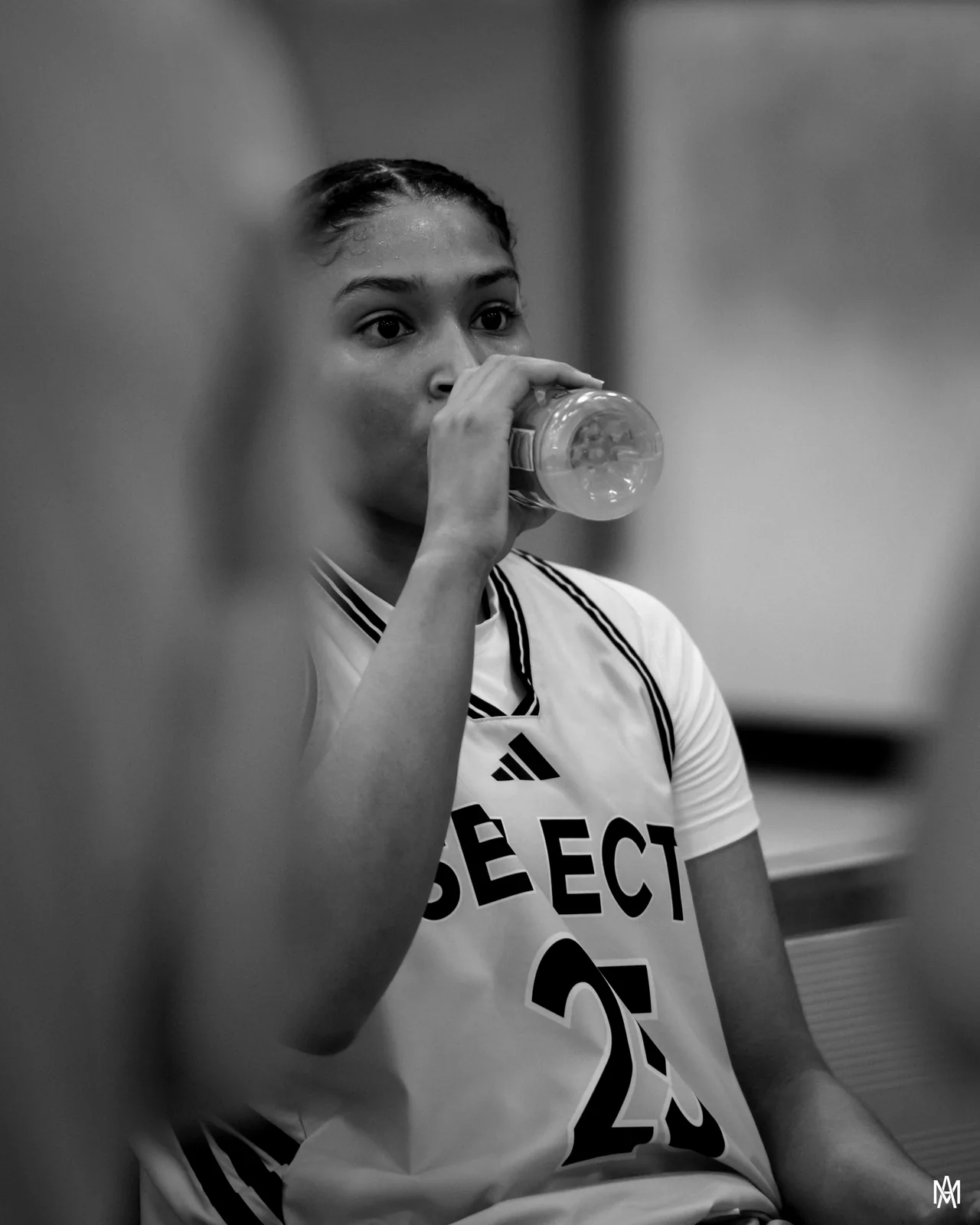 Black and white photo of Amayah Garcia taking a drink on the bench, eyes up on the floor.