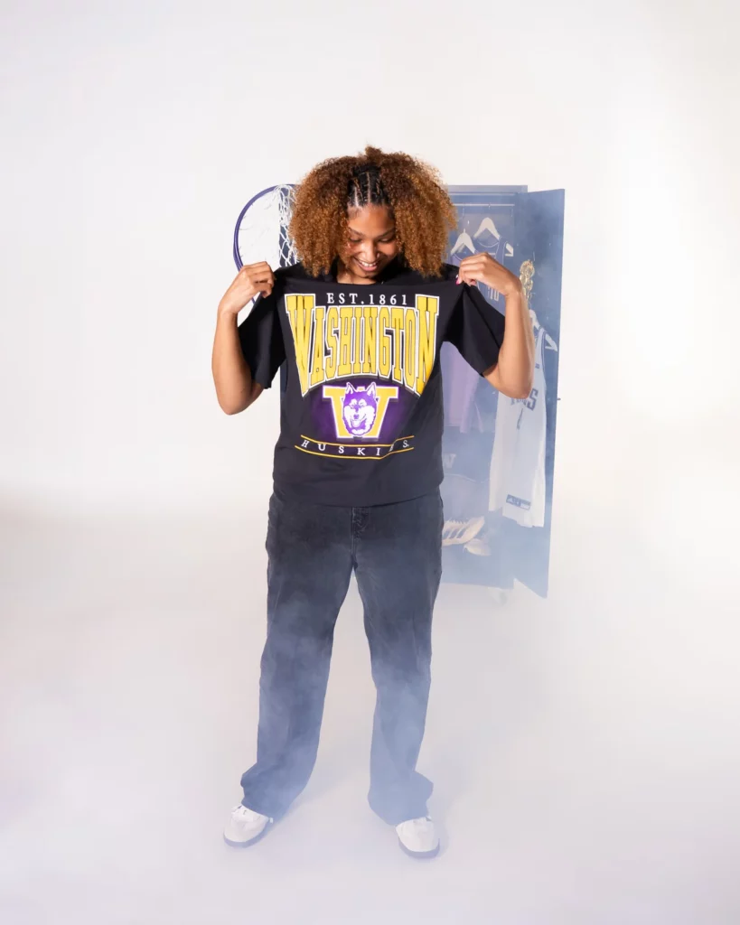 Amayah Garcia holding up a vintage Washington Huskies tee in a studio locker set.